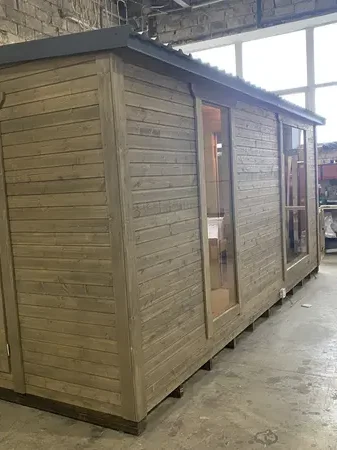 Vue extérieure d’un sauna modulable 5 m peint en gris clair, porte vitrée et grande fenêtre latérale.
