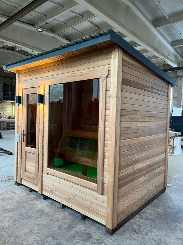 Entrée d’un sauna « L » en bois naturel, porte vitrée ouverte, banquette intérieure visible.