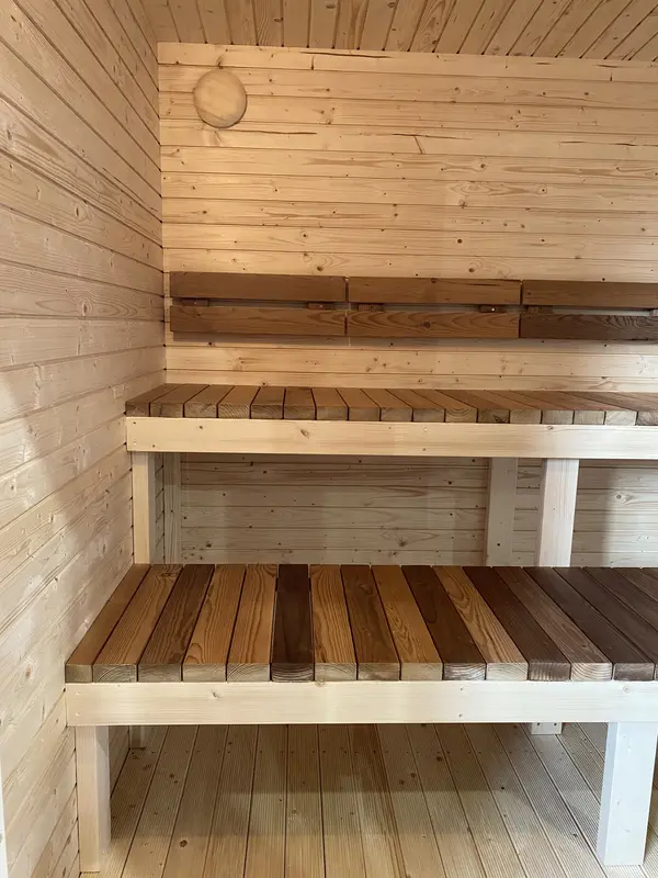 Gros plan sur les deux niveaux de bancs en bois naturel à l’intérieur d’un sauna lambrissé.