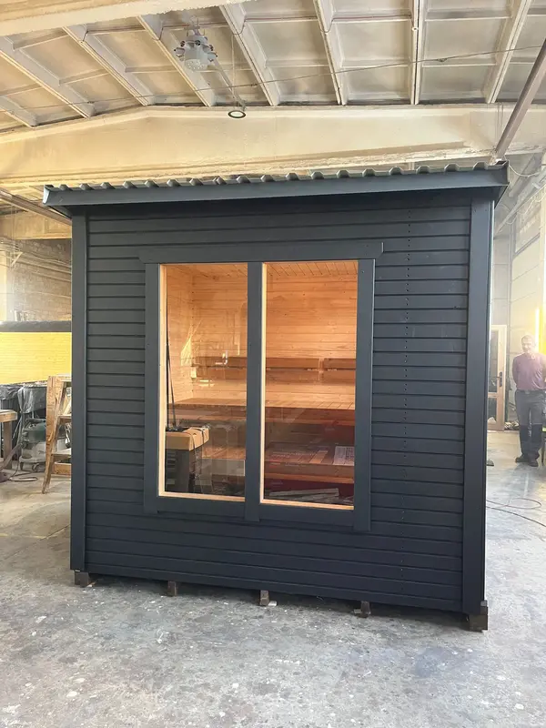 Vue frontale d’un sauna box peint en noir, double porte vitrée laissant entrevoir l’intérieur bois.