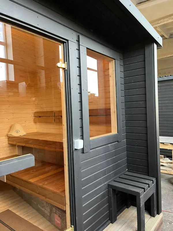 Détail extérieur d’un sauna box noir avec porte vitrée et banquette intérieure aperçue.