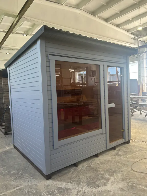 Sauna modulable peint en gris clair, grande fenêtre fixe sur la façade, intérieur bois visible.