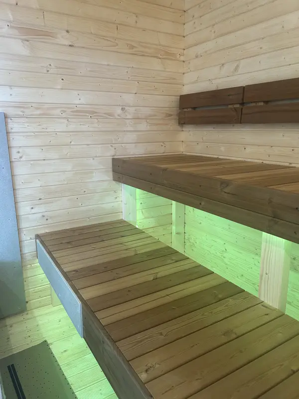 Intérieur de sauna montrant banquettes en bois à deux niveaux éclairées par des LED vertes sous l’assise.