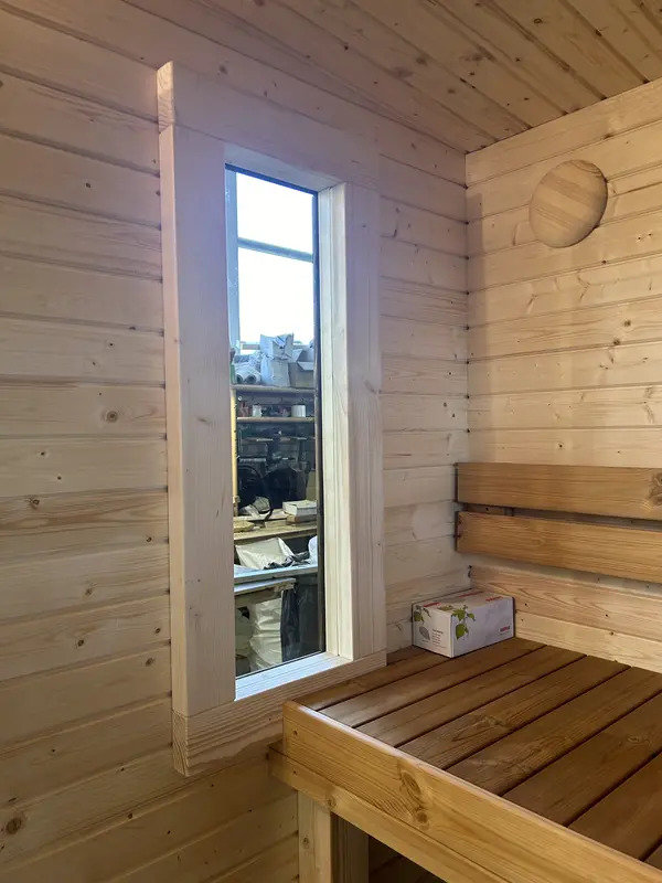 Intérieur d’un sauna « L » en bois naturel, mur lambrissé clair et banc sommier visible.