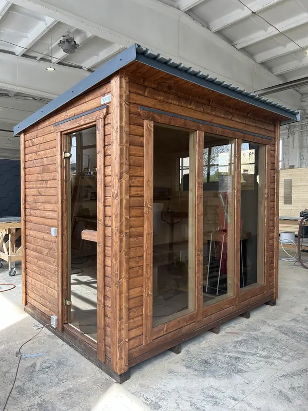 Sauna modulable ThermoWood finition bois naturel en angle, larges baies vitrées sur deux façades, en atelier.