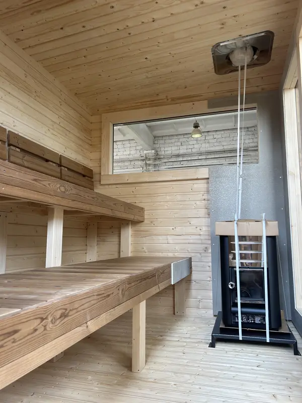 Intérieur de sauna box avec deux niveaux de bancs en bois clair et poêle visible, murs lambrissés.