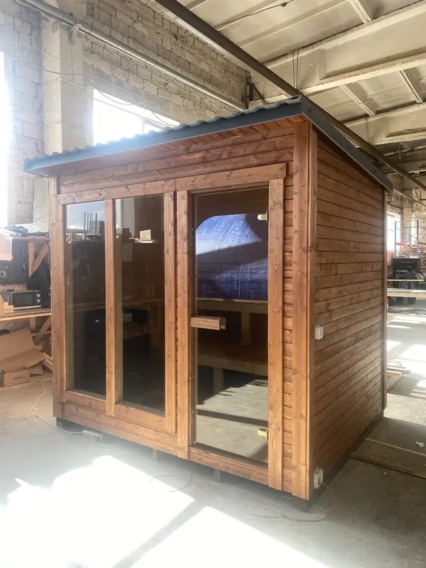 Sauna en caisson ThermoWood finition bois naturel, façade avec double porte vitrée et fenêtres latérales.