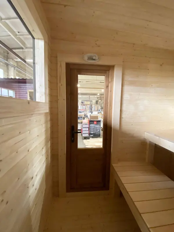 Vue intérieure d’un sauna en bois clair, couloir d’entrée avec mur lambrissé et plafonnier.