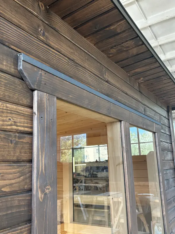 Vue rapprochée d’un angle de sauna « L » en ThermoWood foncé, bordure métallique sur la jonction des murs.