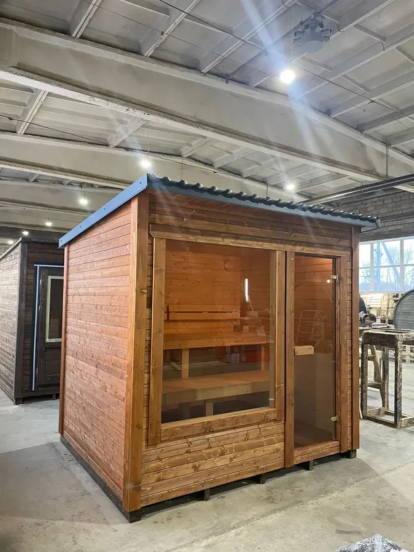 Deux saunas box côte à côte en atelier : un à finition bois naturel devant et un plus sombre derrière.