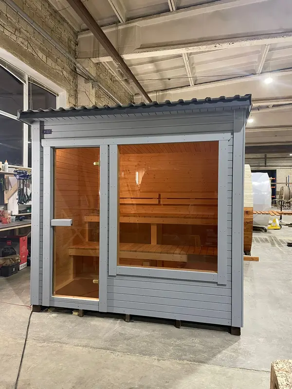 Sauna modulable peint en gris clair, façade vitrée laissant entrevoir les banquettes en bois.