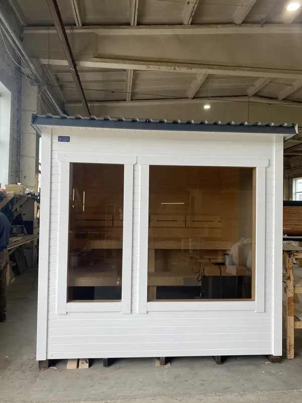 Façade avant d’un sauna modulaire peint en blanc, double porte vitrée et toit légèrement incliné.