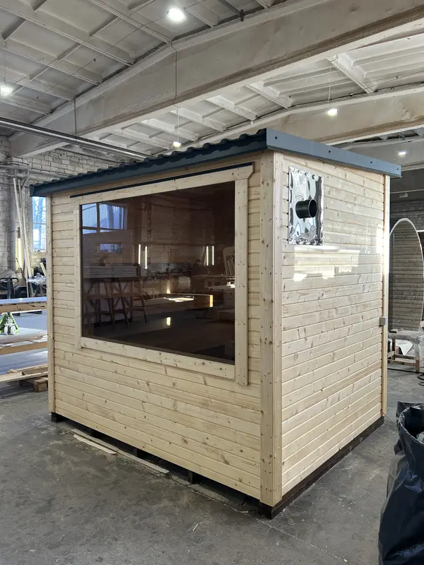 Sauna modulable en configuration « L » en bois clair, grande fenêtre panoramique et mur latéral, en atelier.