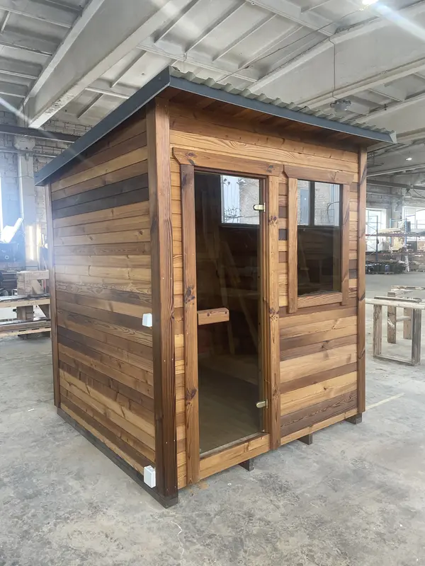 Sauna box ThermoWood finition bois naturel, vue frontale avec double porte vitrée et fenêtre latérale, intérieur prosté visible.