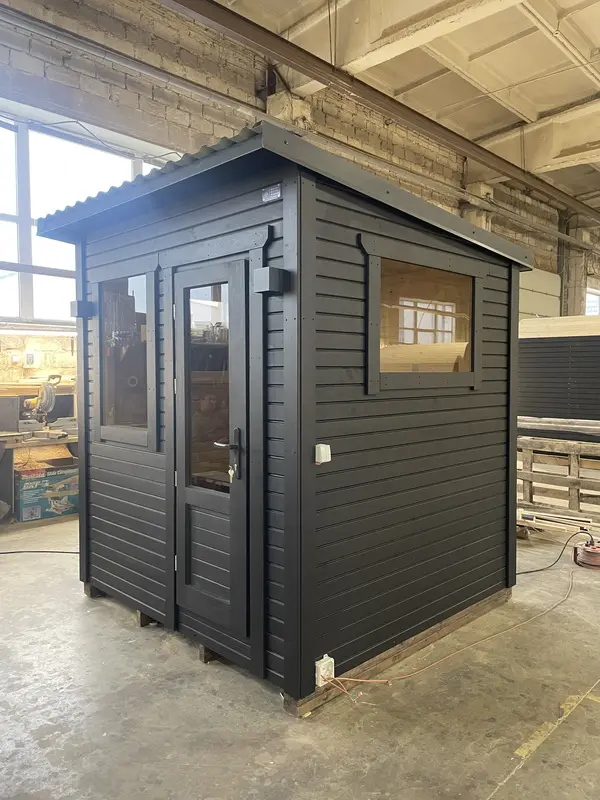 Sauna box noir d’angle à double porte vitrée et petit châssis latéral, en hangar.