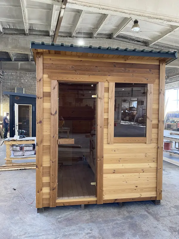 Sauna box ThermoWood brut, vue frontale avec porte vitrée et fenêtre à côté, bardage à lames large.