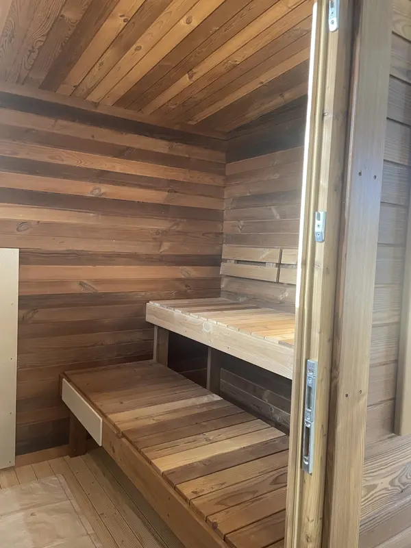 Intérieur de sauna box avec mur lambrissé brun et deux niveaux de bancs en bois naturel.