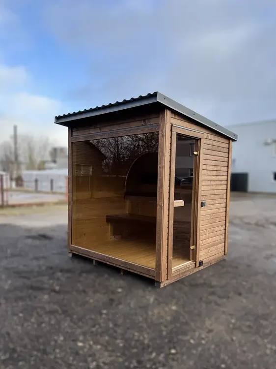 Sauna box ThermoWood peint en noir avec grande fenêtre frontale et toit incliné, en extérieur.