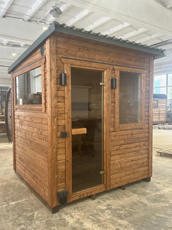 Sauna modulaire ThermoWood finition bois naturel avec porte vitrée et fenêtre latérale, posé sur palettes en intérieur.