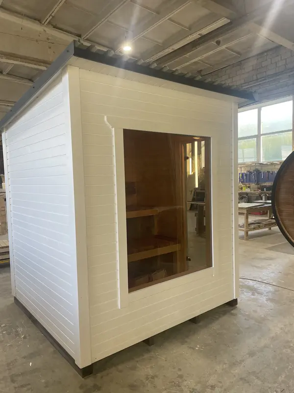 Intérieur de sauna box peint en blanc vu à travers une large fenêtre, murs lambrissés et banc en bois.
